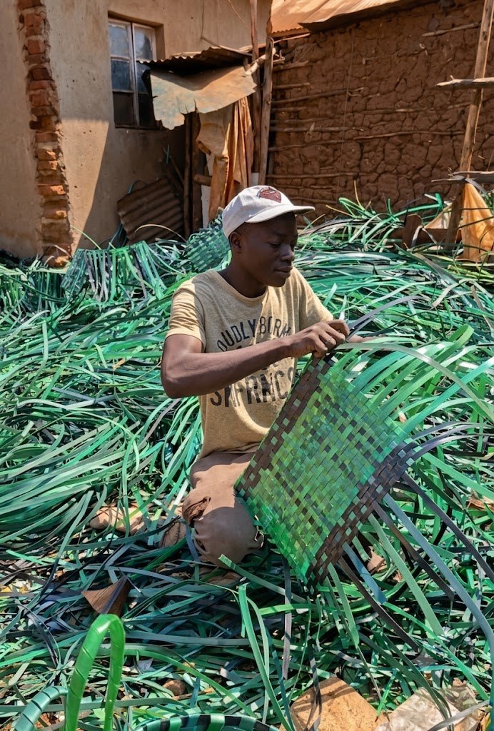 A young weaver completing a handmade basket in Busia District