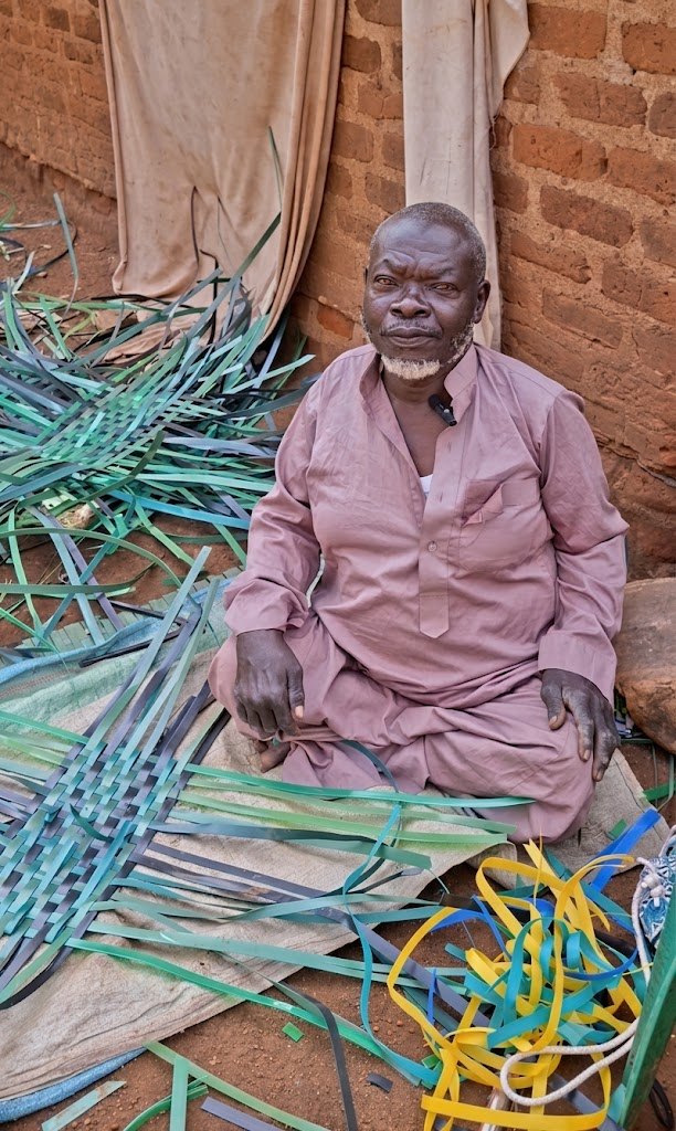 Issa preparing woven strips for a basket outside his home in Mawero, Busia